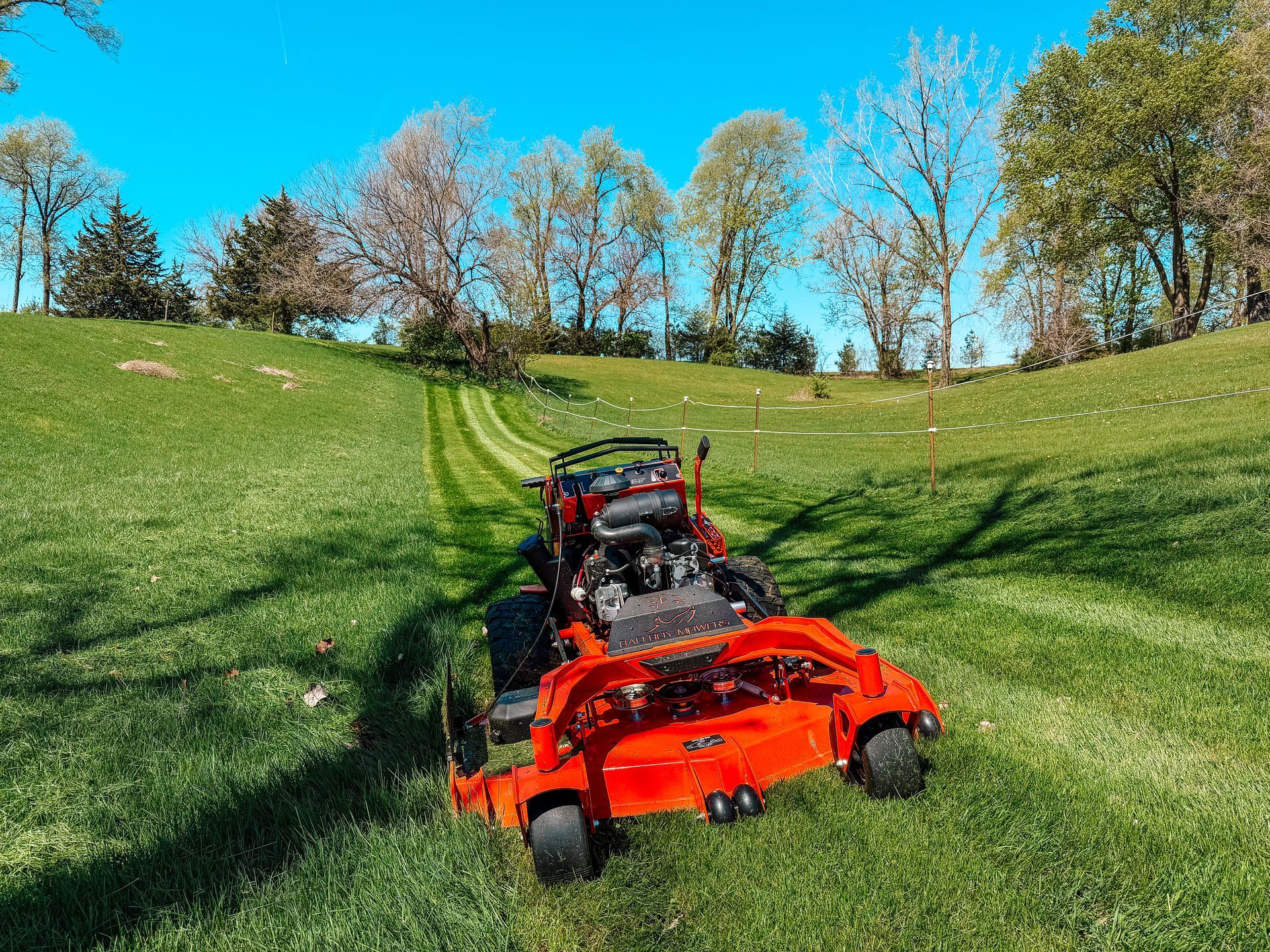 Orange mower cutting grass on a sunny green hillside