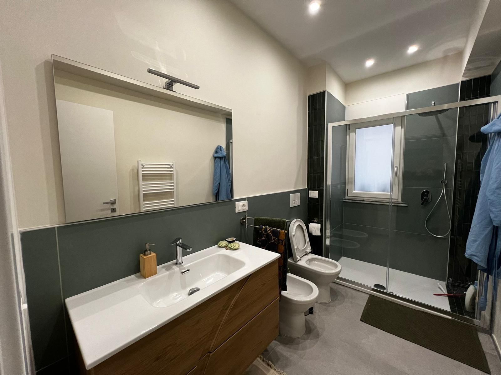 Un bagno con lavandino, water, doccia e specchio.
