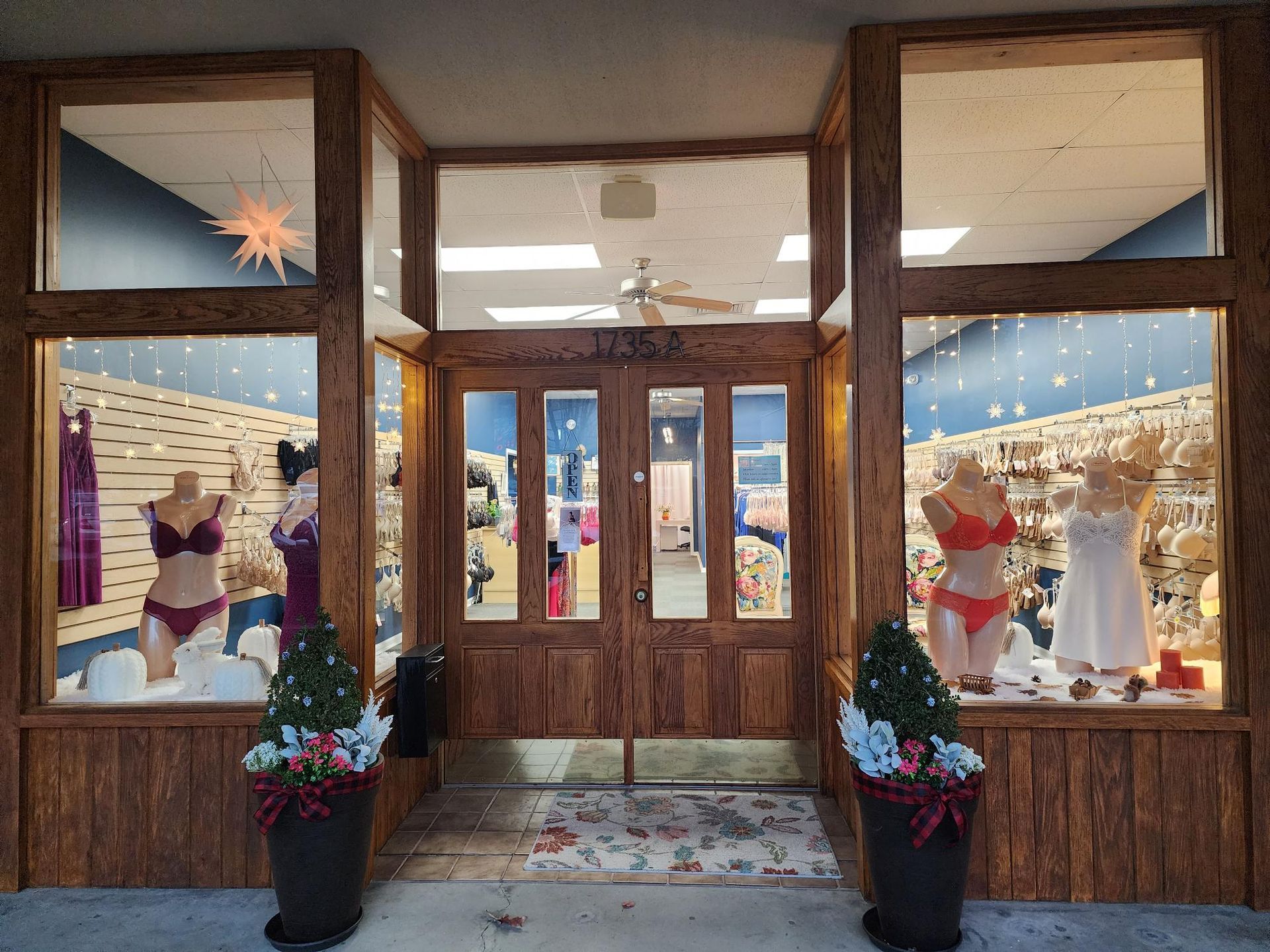 Wooden storefront with holiday window displays, festive decorations, and lights around the entrance.