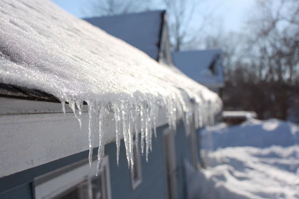 Toit enneigé avec des stalactites de glace pendant du bord d'une maison bleu clair par une journée ensoleillée.
