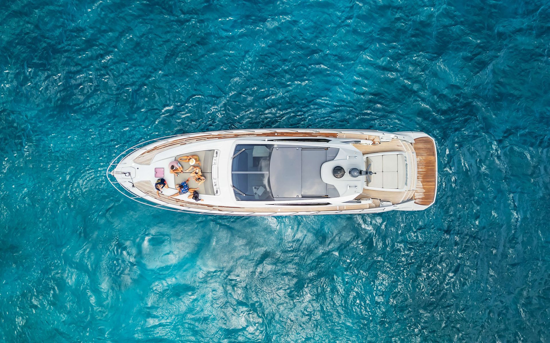 White yacht on blue ocean, overhead view. People sunbathing on deck.