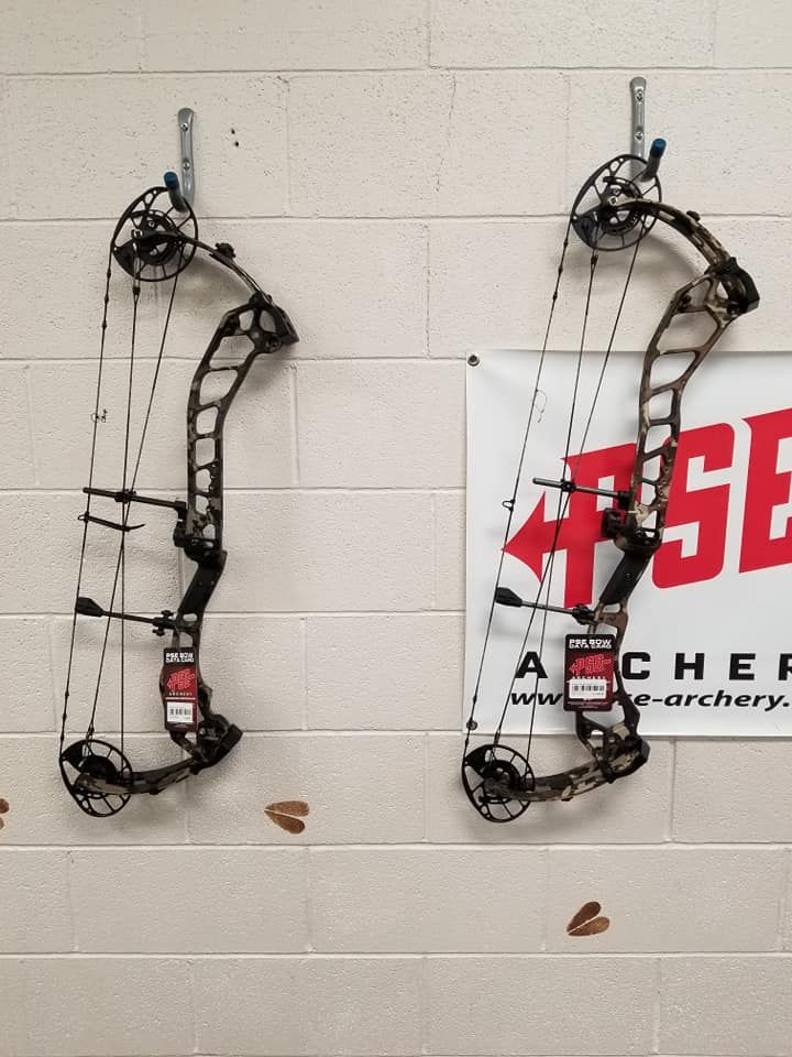 Two compound bows hanging on a cinderblock wall beside a target poster.