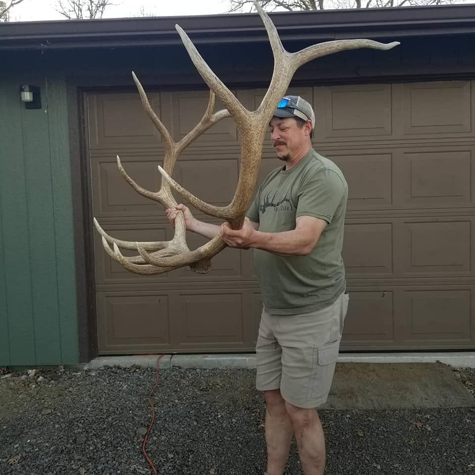 Man holding a large antler rack in front of a garage