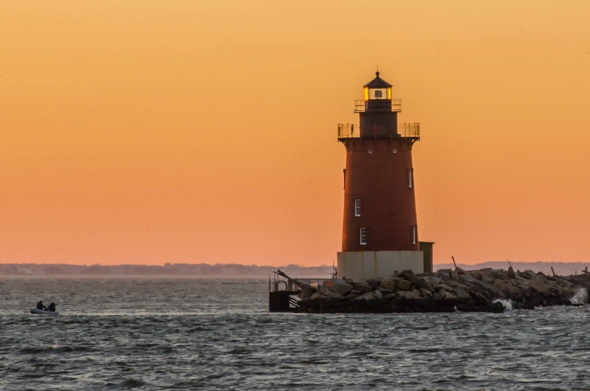 Two boaters are shown near the Delaware Breakwater East End Lighthouse on Delaware Bay at sunset.