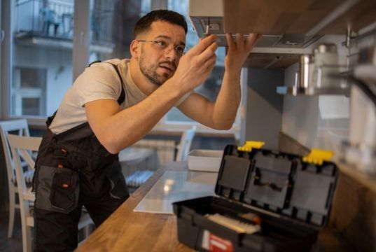 A man is working on a stove in a kitchen.