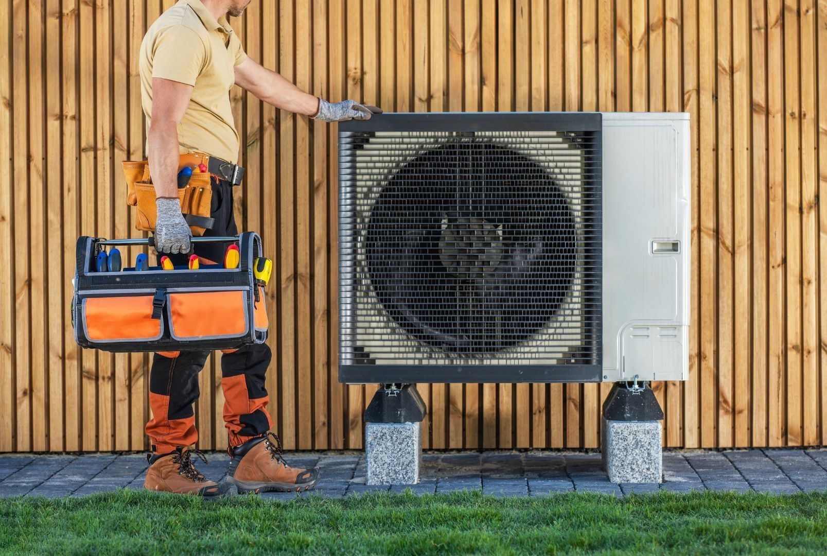 A man is holding a toolbox in front of an air conditioner.