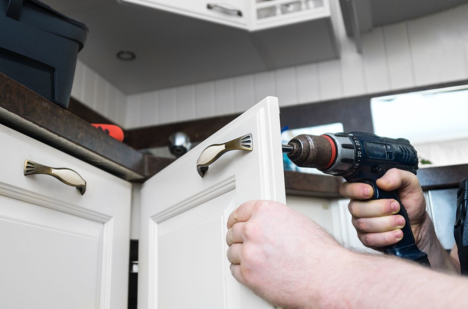 A person is fixing a kitchen cabinet with a drill.