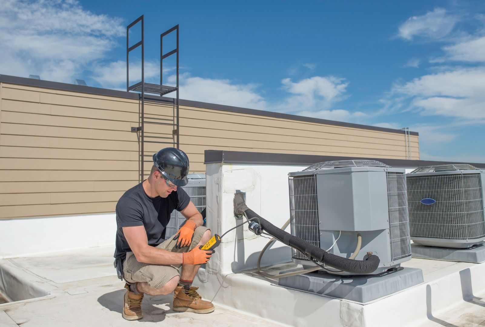 A man is working on an air conditioner on the roof of a building.
