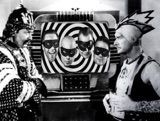 A black and white photo of two men standing next to each other in front of a television.