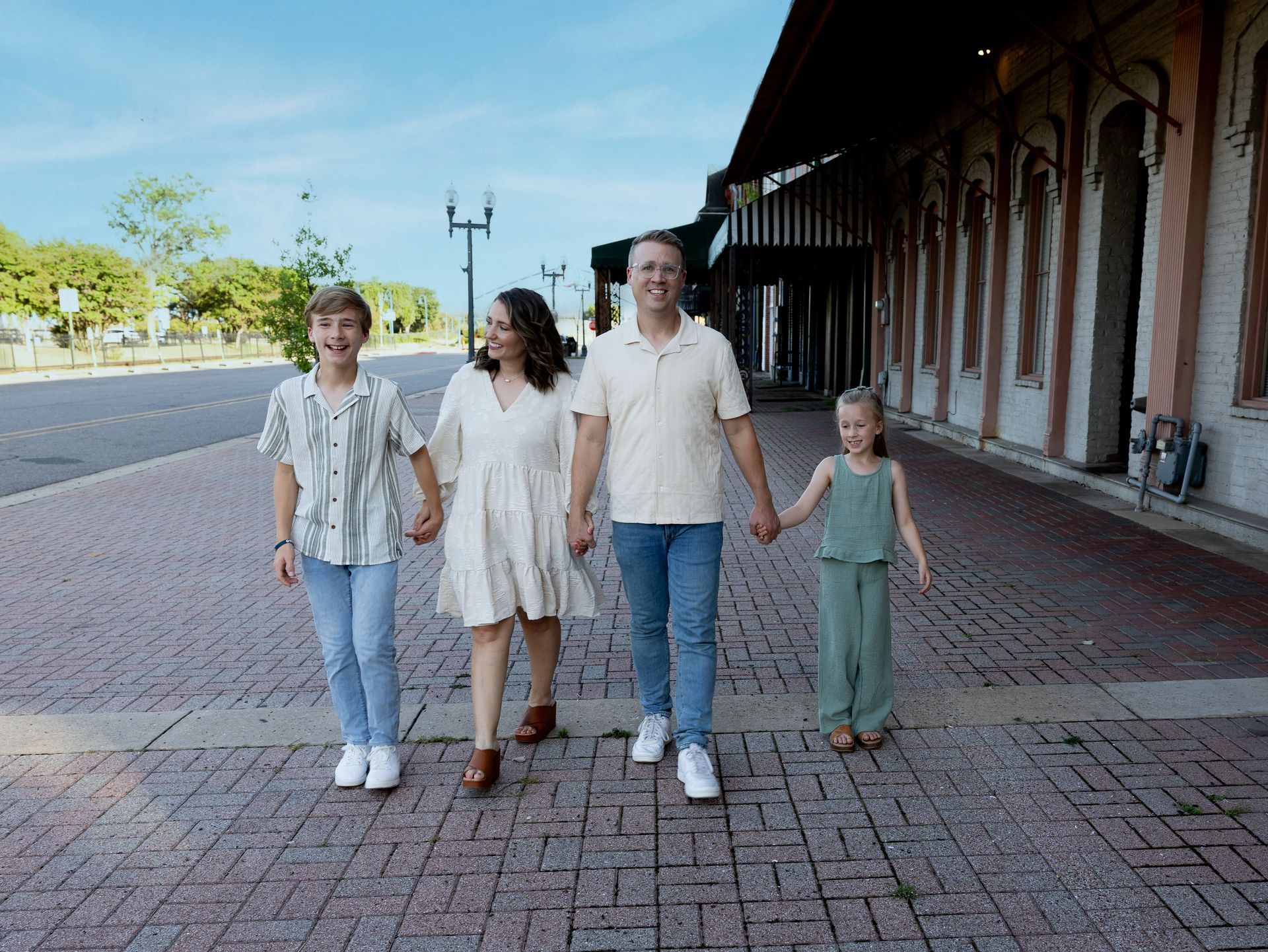 Four people walking hand in hand along a brick sidewalk beside a building