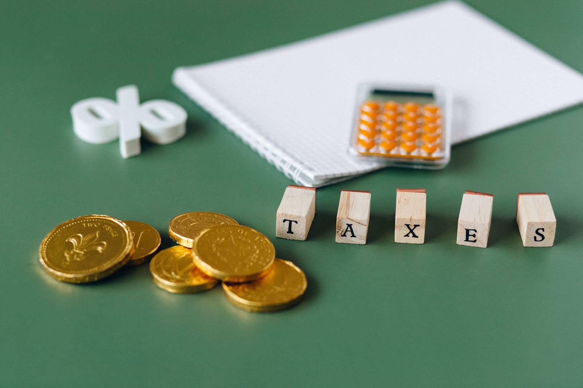 Tax items beside coins, calculator, notebook, and paper clips on a green desk