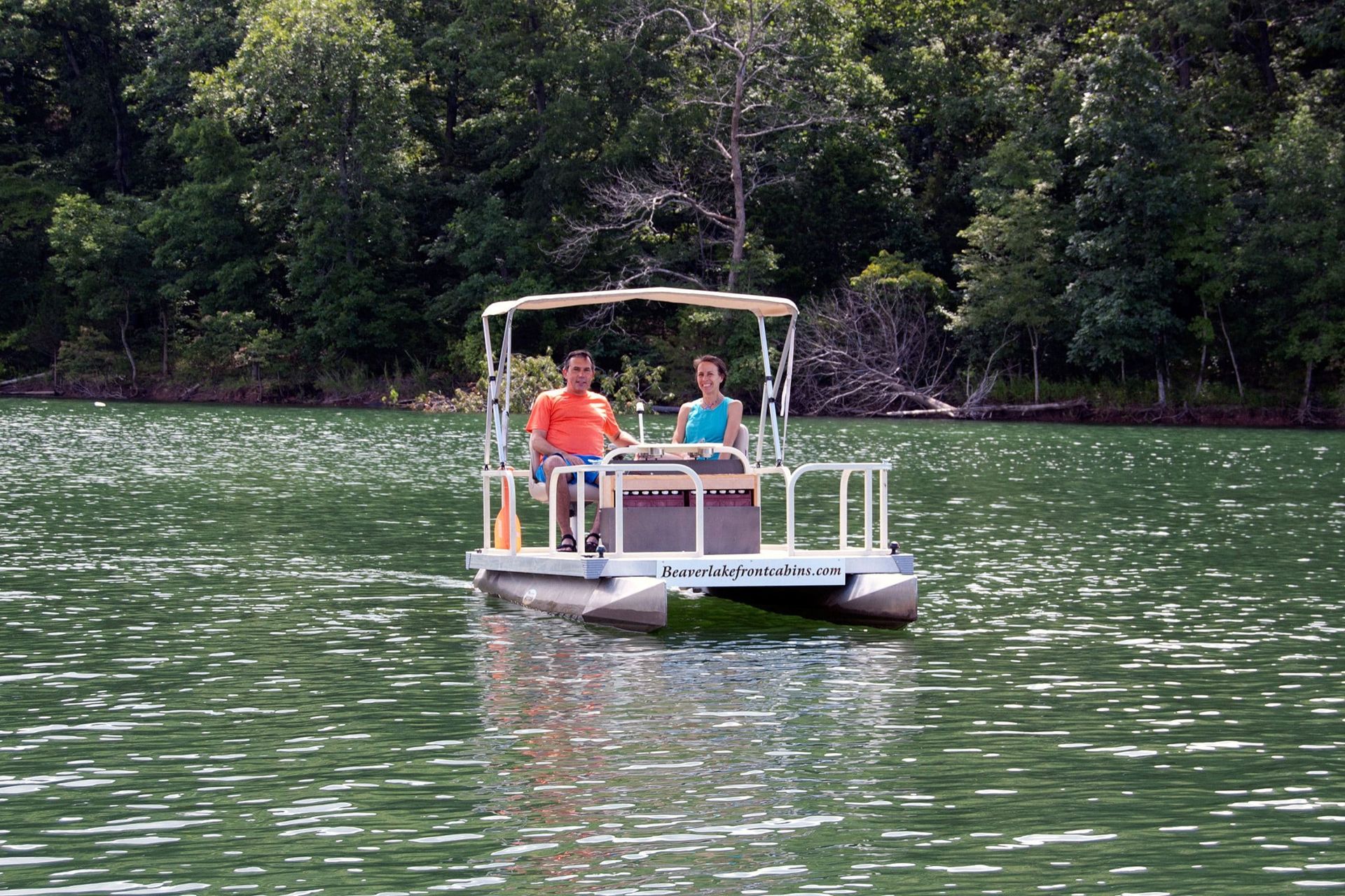 Two people are riding a pontoon boat on a lake.