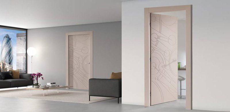 Interno minimalista con due porte bianche aperte e un divano grigio in una stanza luminosa.