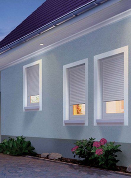 Esterno di una casa blu con tre finestre incorniciate di bianco e piccole aiuole lungo il muro.