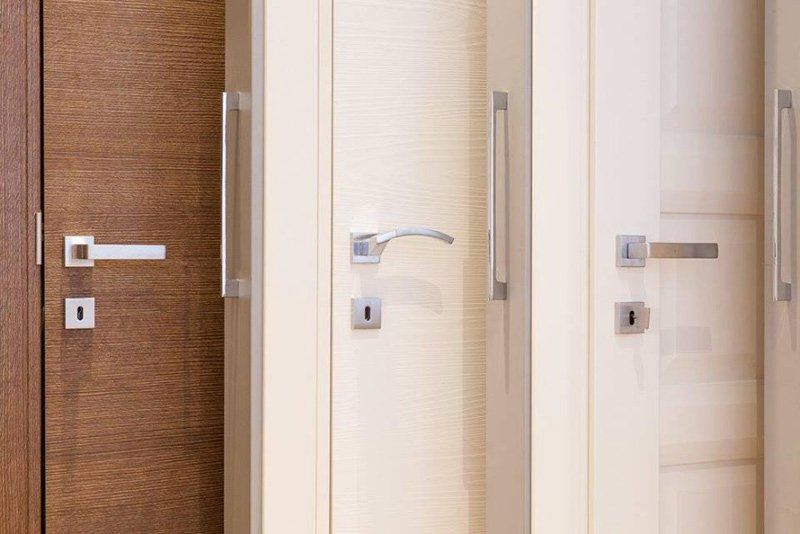 Fila di porte interne moderne con finiture in legno bianco e marrone e maniglie argentate.