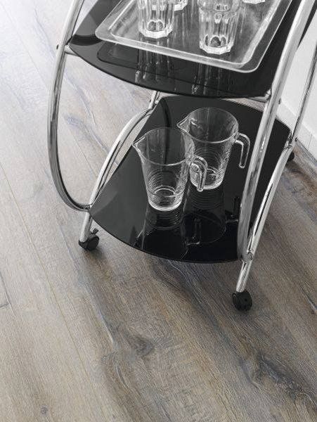 Piccolo carrello nero su ruote, posizionato su un pavimento di legno, con contenitori di plastica trasparente sugli scaffali.
