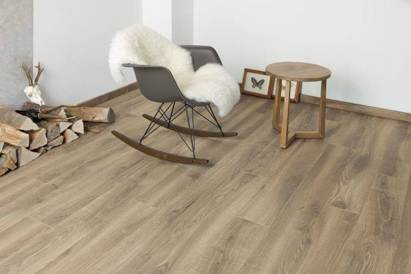 Soggiorno moderno con sedia a dondolo, tavolino e catasta di legna su pavimento effetto legno.