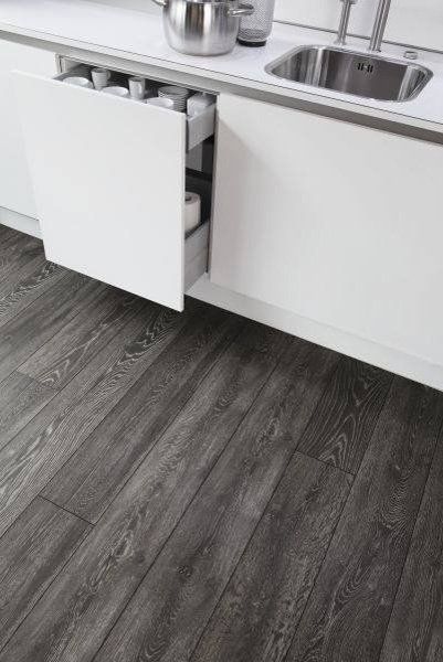 Cucina moderna con mobili bianchi, lavello in acciaio inox e pavimento effetto legno scuro.