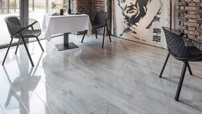 Moderno loft-caffetteria con tavolo con tovaglia bianca, sedie nere e un grande ritratto a parete su pavimento bianco.