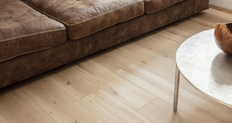 Divano marrone accanto a un tavolino rotondo bianco su un pavimento in legno chiaro.