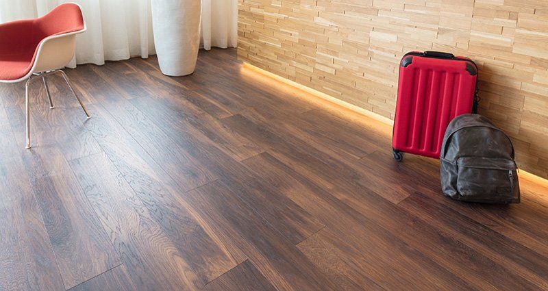 Pavimento in legno vicino a un muro di mattoni con una valigia rossa, uno zaino nero, una sedia e delle tende.
