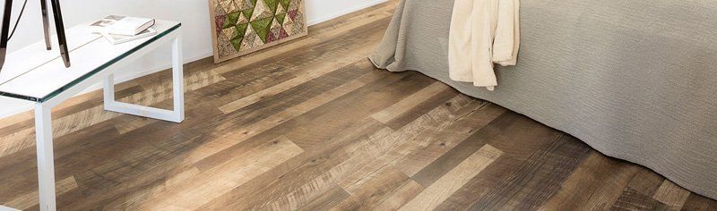 Accogliente angolo camera da letto con pavimento in legno, letto, tavolino bianco e una piccola pianta vicino alla finestra.