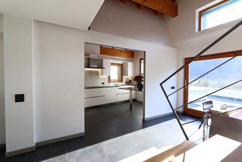 Cucina e zona pranzo luminose e moderne con pareti bianche, pavimento scuro e ampie finestre con vista sulle montagne.