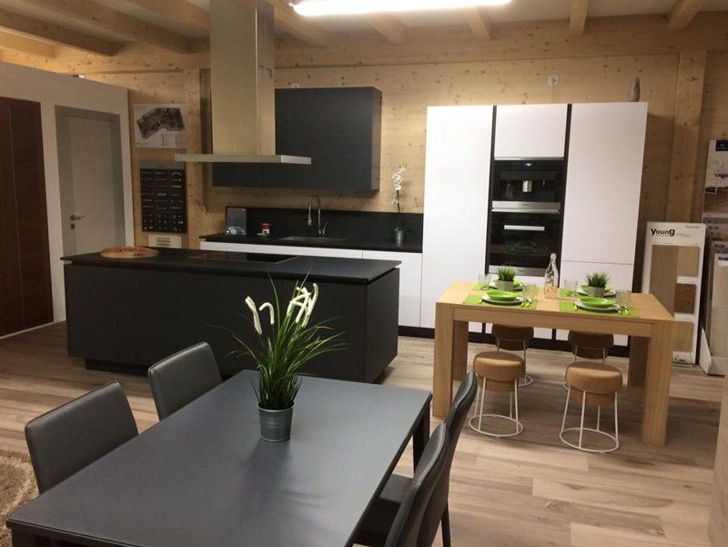 Cucina e zona pranzo moderne a pianta aperta con isola nera, dettagli in legno e tavolo apparecchiato con piante.