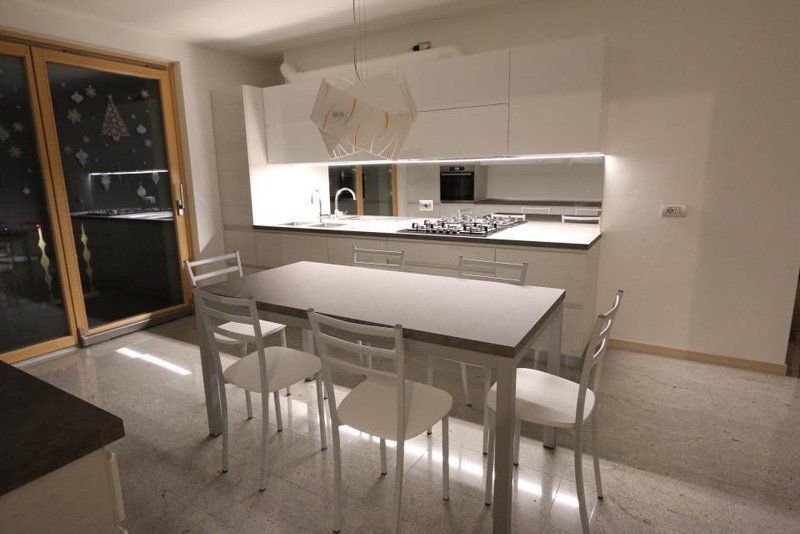Cucina moderna e zona pranzo con tavolo e sedie bianchi e grande finestra di notte