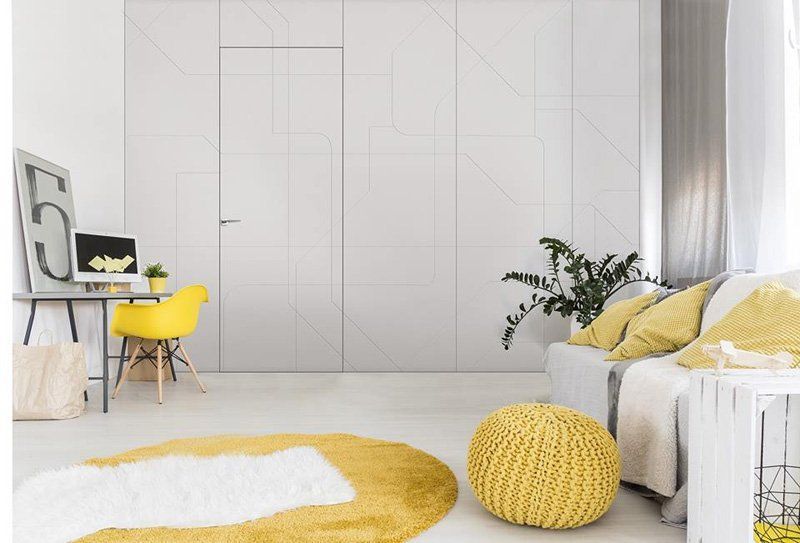 Luminoso soggiorno minimalista con poltrona, divano, tappeto e pouf gialli sullo sfondo di armadi a muro bianchi.