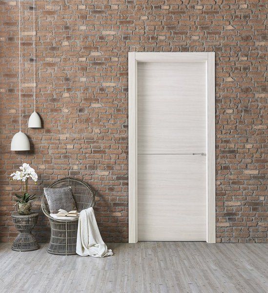 Stanza minimalista con parete in mattoni a vista, porta bianca, sedia in vimini, fiori e lampade a sospensione.