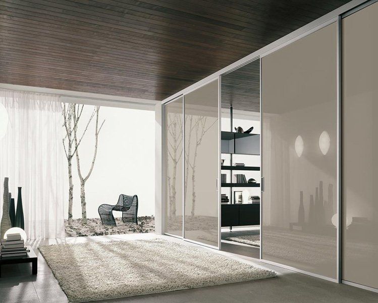 Interni moderni e minimalisti con pareti in vetro, poltrona e patio soleggiato con alberi all'esterno.