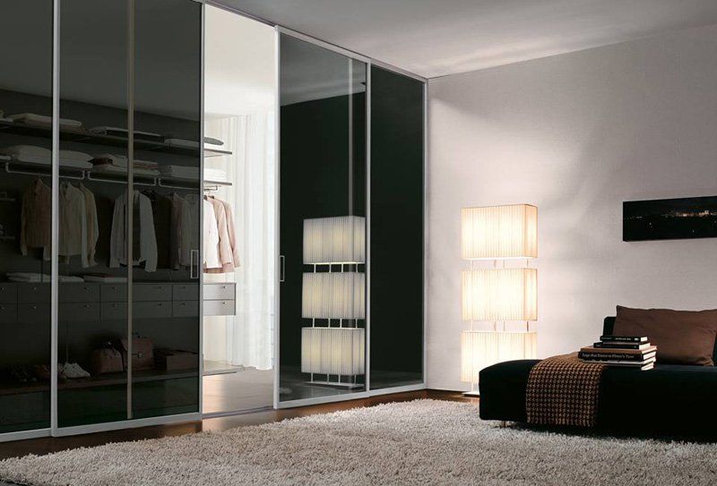 Camera da letto moderna con ante scorrevoli scure dell'armadio, pareti bianche, letto, tappeto e lampade da terra alte.