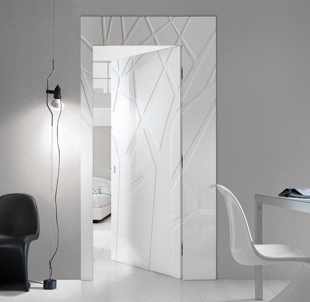 Interno bianco con porta a giorno decorata, sedia nera, lampada da terra e scrivania bianca sulla destra.