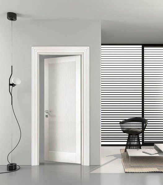 Stanza minimalista grigia con porta bianca aperta, lampada da terra e sedia accanto a una finestra a righe.