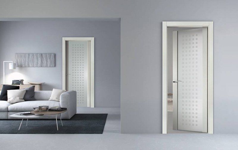Soggiorno moderno con divano grigio e due porte bianche aperte che conducono a una stanza luminosa.