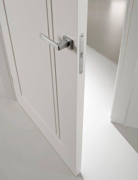 Una porta bianca socchiusa con maniglia argentata lascia intravedere una stanza luminosa al di là.