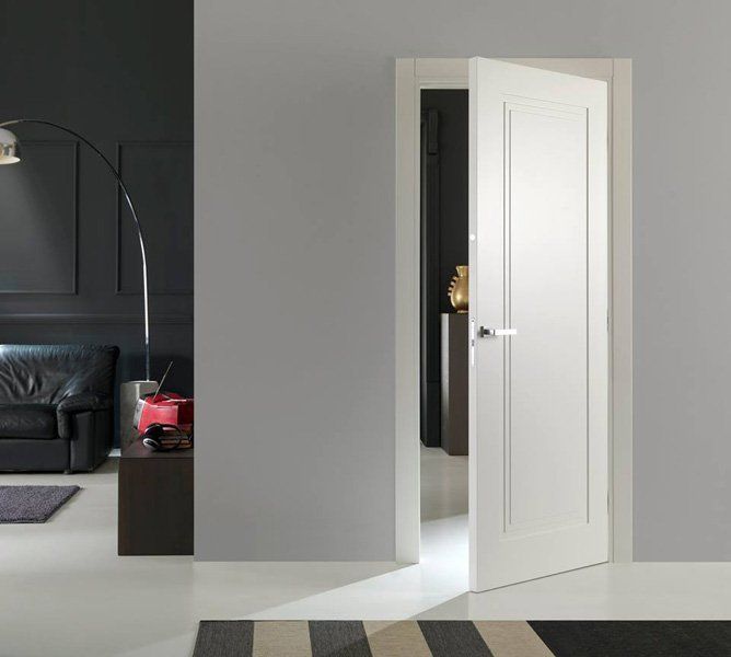 Una porta bianca si apre su un soggiorno grigio con un divano nero e un tappeto a righe.