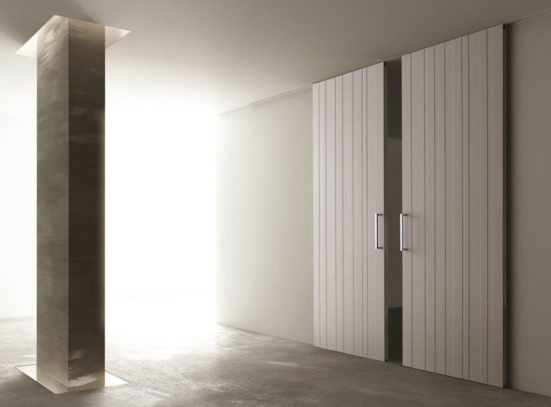 Corridoio moderno e minimalista con luce naturale, pavimento in cemento e alte doppie porte a pannelli bianchi.