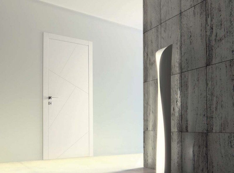 Interno minimalista con porta bianca e parete rivestita di piastrelle grigie accanto a un pannello curvo simile a uno specchio.