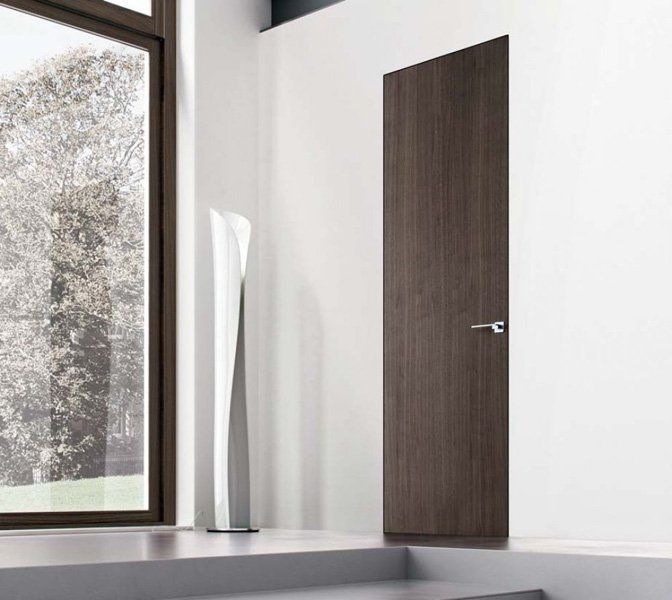 Bagno moderno e minimalista con porta in legno scuro, pareti bianche e un'ampia finestra satinata.