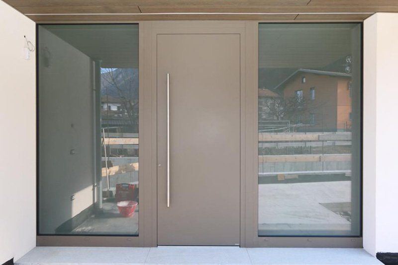 Moderne doppie porte d'ingresso in vetro con pannello centrale pieno, viste dall'esterno.