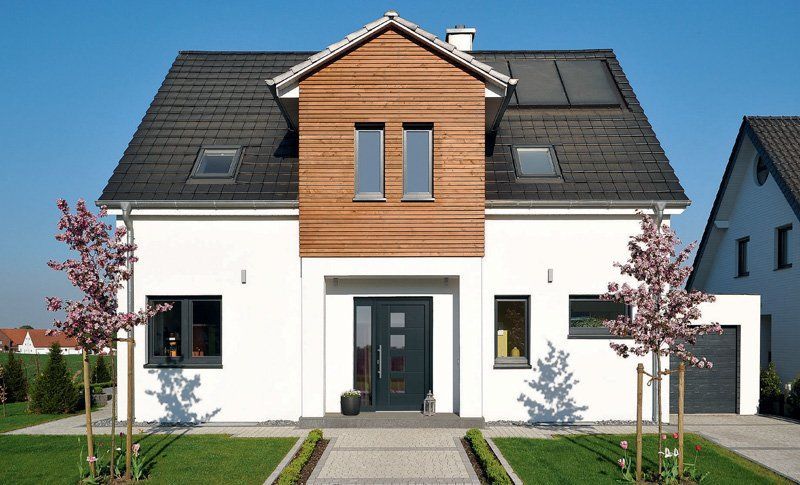 Casa moderna a due piani con facciata bianca, dettagli in legno, tetto scuro e vialetto d'ingresso fiancheggiato da piccoli alberi.