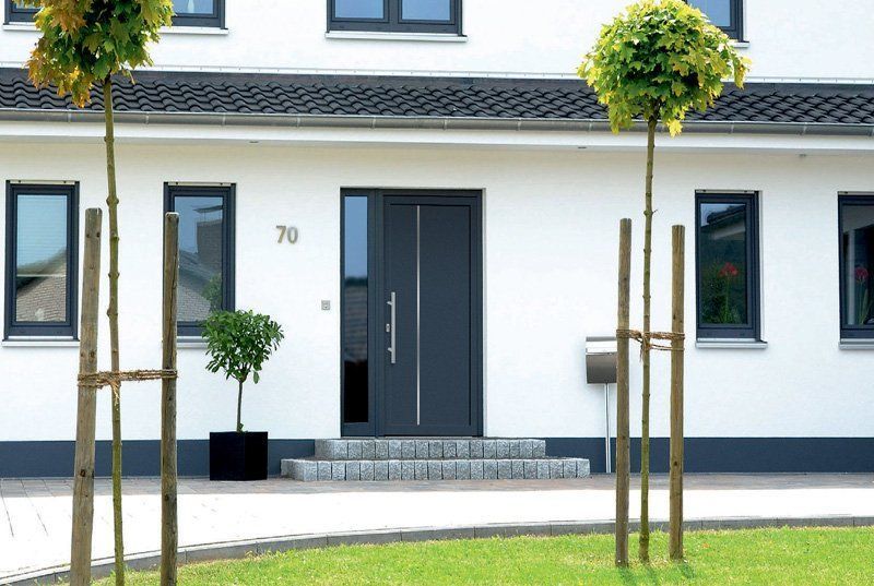 Esterno di una moderna casa bianca con porta e finestre nere e piccoli alberi nel giardino anteriore.