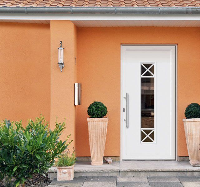 Porta d'ingresso bianca con finestre strette, fiancheggiata da piante in vaso su una parete intonacata color pesca.
