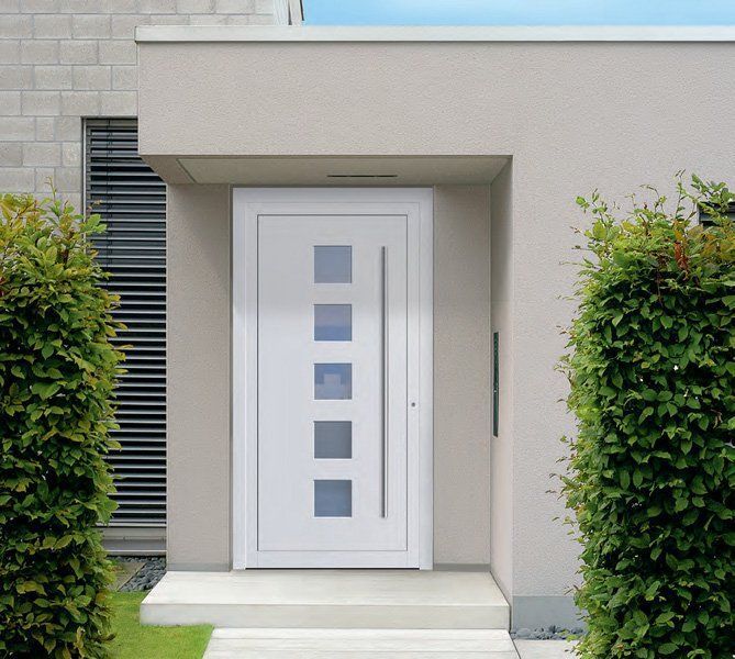 Porta d'ingresso moderna con pannelli di finestre quadrati, incorniciata da pareti beige e arbusti verdi