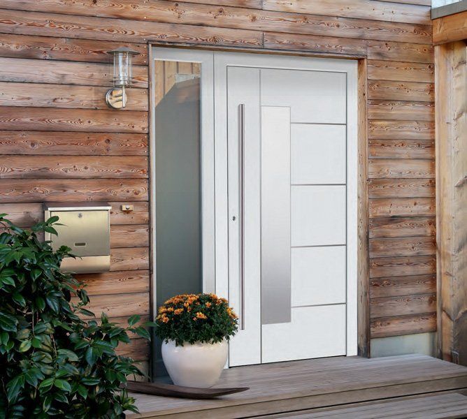 Porta d'ingresso bianca con vetro satinato su una casa di legno, accanto a un vaso di fiori e una lanterna da parete.
