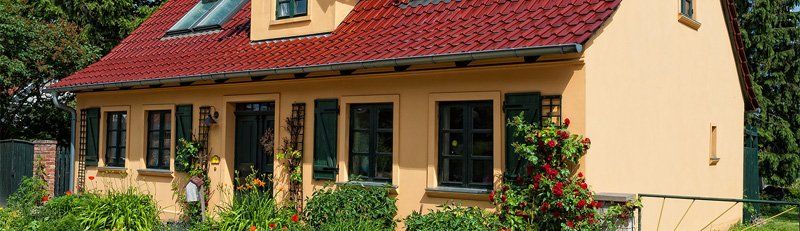 Casa a un solo piano con tetto di tegole rosse, pareti beige e giardino anteriore soleggiato