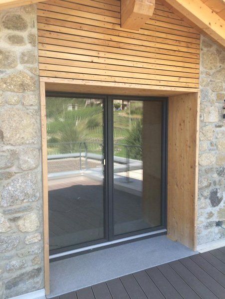 Ingresso con muro in pietra, porta scorrevole in vetro e tettoia a lamelle in legno.