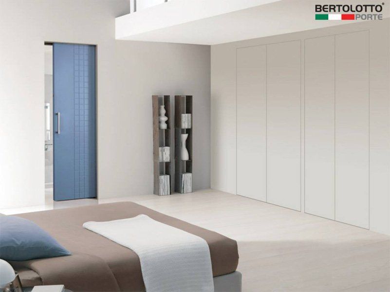 Camera da letto moderna con porta blu, letto beige e ampi armadi a muro bianchi.